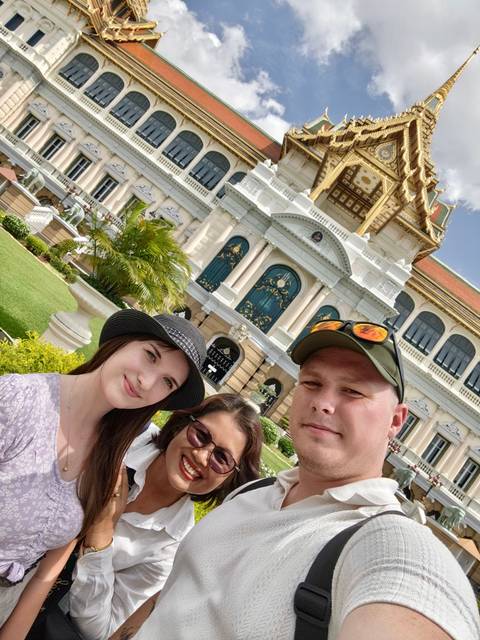 Selfie of three travellers in front of the ornate Grand Palace buildings in Bangkok.