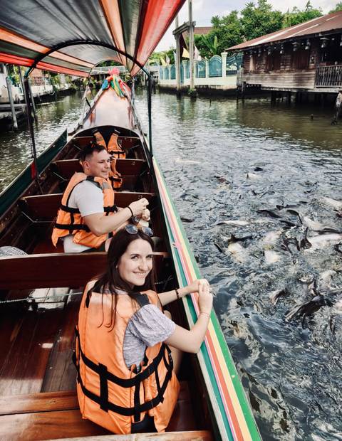 Couple in a long-tail boat feeding a frenzy of fish in the water.