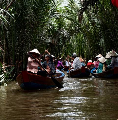 Multiple sampans rowed by locals wearing conical hats through dense nipa palms.