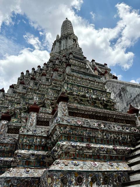 Upward perspective of an ornately tiled temple tower against partly cloudy skies.