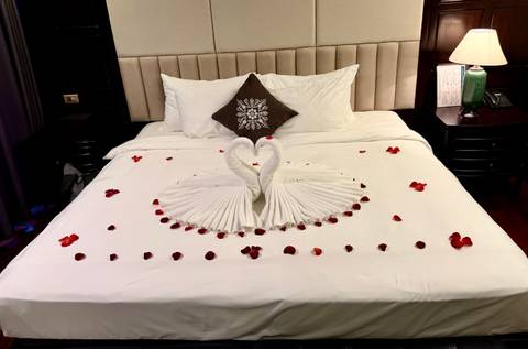 Hotel bed decorated with towel swans and rose petals for a romantic setup.