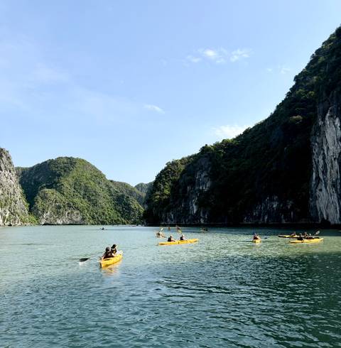 Kayakers paddle through emerald waters surrounded by towering limestone cliffs in Ha Long Bay.