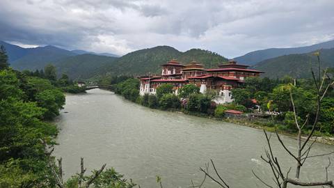 The riverside Punakha Dzong monastery-fortress framed by lush greenery with misty mountains beyond a wide gray river.