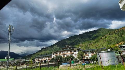 Valley town in Bhutan beneath dark storm clouds with green hills rising behind