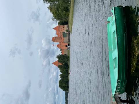 Red-roofed medieval castle complex viewed across a calm lake under grey skies