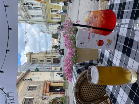 Outdoor café table with beer and Campari spritz overlooking a charming European street and pink flowers