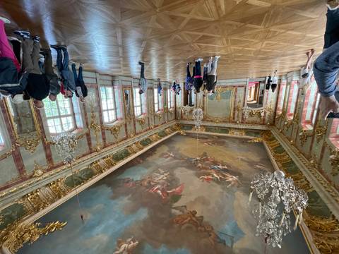 Lavish baroque ballroom with ornate gold details and painted ceiling where tourists admire the decor