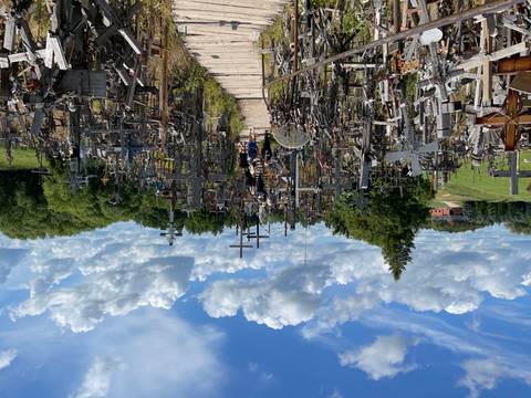 Pathway densely lined with thousands of wooden crosses against a vivid blue cloud-dotted sky