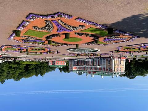Formal palace gardens with patterned flowerbeds, fountain and cyclists under bright summer sky