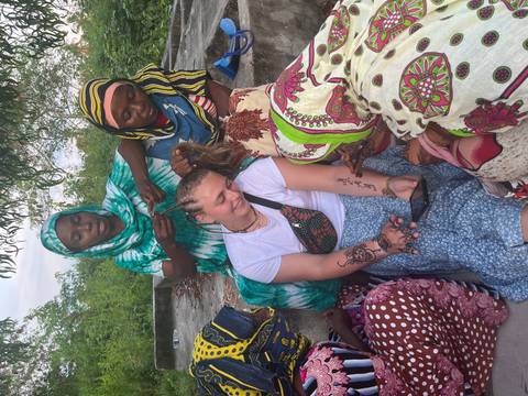 Traveller smiles while local women braid her hair in an outdoor setting