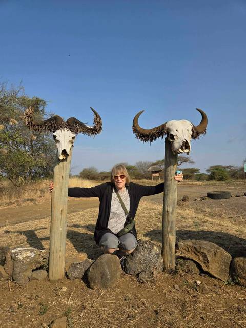 Traveler poses between two mounted buffalo skulls on wooden posts in a dry bush landscape.