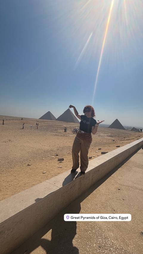 Tourist playfully posing with distant pyramids on a sunny desert plateau