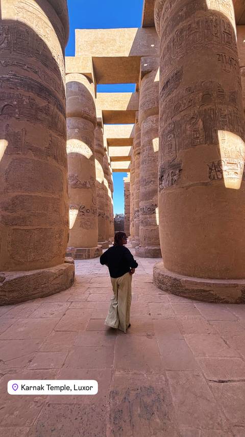 Person walking among massive hieroglyph-covered columns in an ancient temple