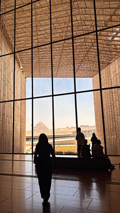 View of pyramids through large museum window with silhouetted visitors