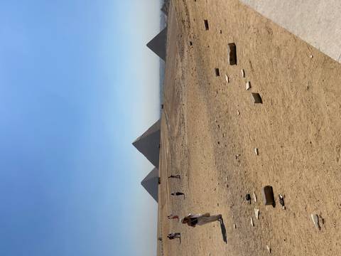 Wide desert expanse with three pyramids on the horizon and scattered tourists
