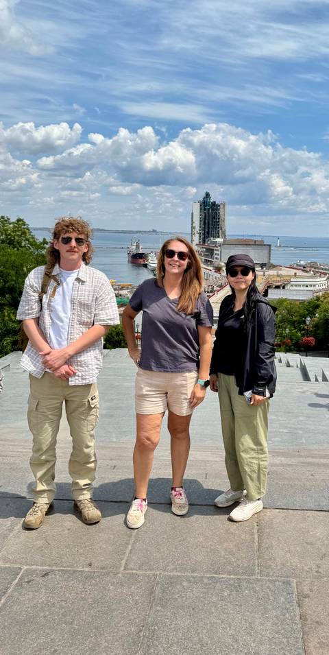 Three travelers pose on wide stone steps overlooking Odesa port and anchored ships.
