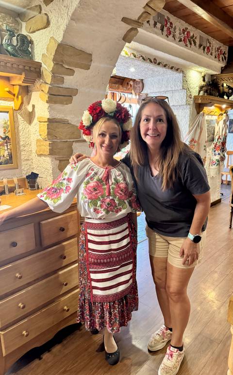 Visitor stands with a woman in ornate Moldovan folk costume inside a rustic restaurant.