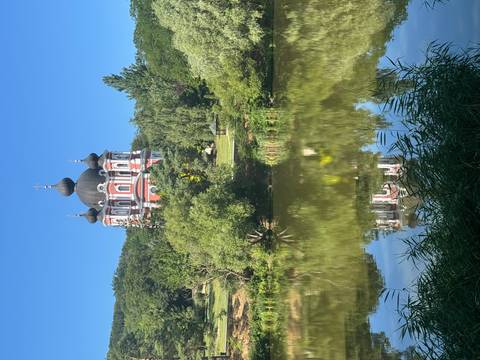 Picturesque domed Orthodox church rises above trees and reflects perfectly in a calm pond.