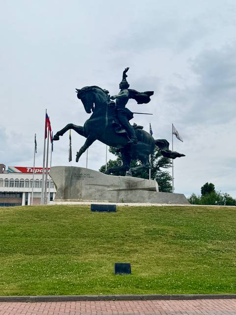 Large bronze equestrian statue on a stone plinth with flagpoles nearby