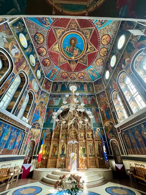 Ornately decorated orthodox church interior with colorful frescoes and chandelier
