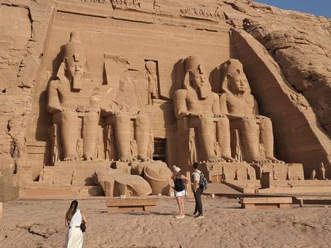 Massive seated statues of Ramses II at Abu Simbel temple with tourists admiring the façade under warm light.