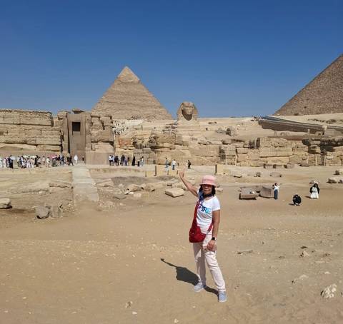 Tourist pointing toward the Sphinx with three Giza pyramids towering in the desert behind.