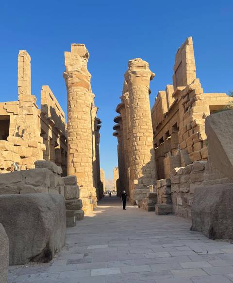 Massive sandstone columns of Karnak Temple lined in sunlight with visitors walking down the avenue.