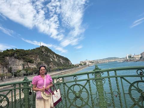 A woman in pink poses on Budapest's green Liberty Bridge overlooking the Danube with Gellért Hill in the background.