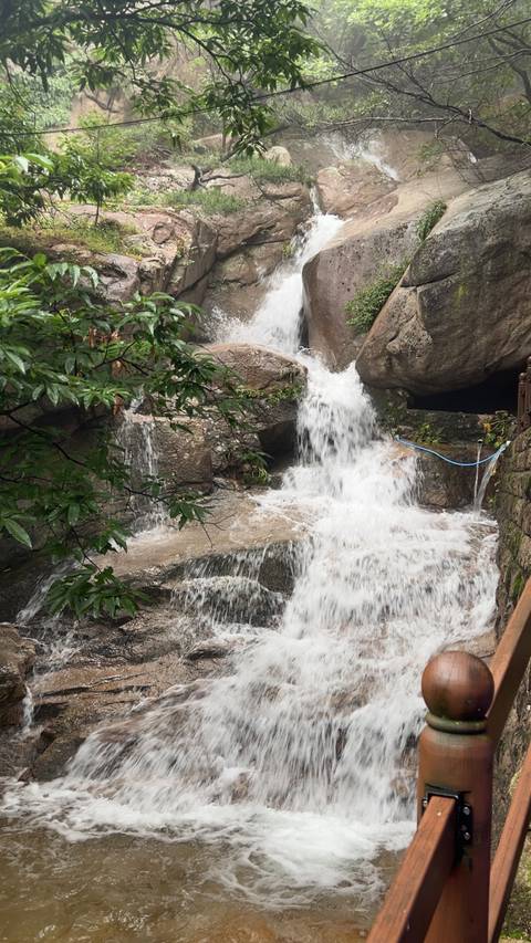 A powerful waterfall tumbles over dark rocks surrounded by green foliage.