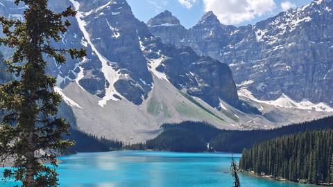 Crystal-clear Moraine Lake reflects snow-streaked peaks and dark evergreens under a brilliant blue sky.