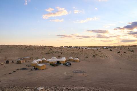 Wide desert camp with rows of white yurts under a pastel sunset sky.