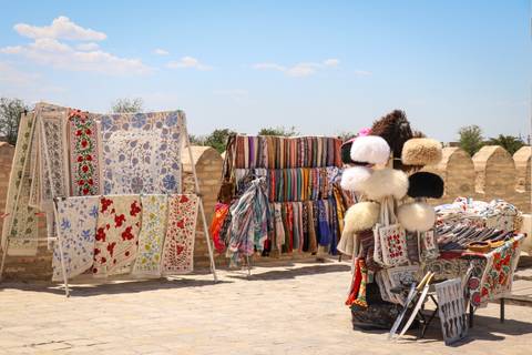 Open-air market stall displaying colorful textiles, scarves and traditional hats against old stone walls.