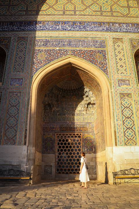 Intricately tiled archway of a Central Asian madrasa catching dramatic light and shadow.