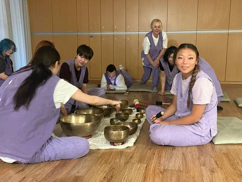 Participants in matching purple attire explore Tibetan singing bowls during an indoor workshop.