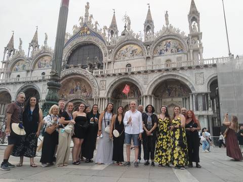 Group stands before ornate façade of St. Mark's Basilica in Venice.