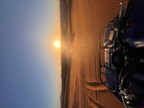 An ATV faces glowing desert dunes while sun rays stream across the sandy landscape at sunset.