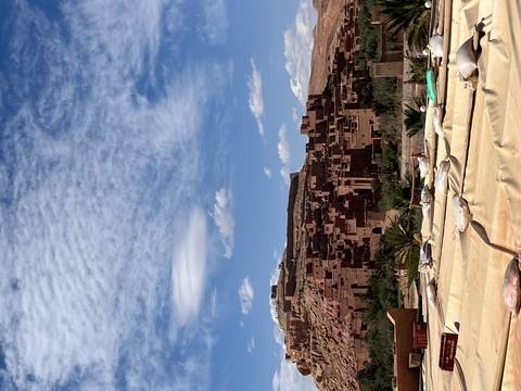 Mud-brick kasbah structures of Ait Benhaddou sprawl beneath a vivid blue sky with dramatic clouds.