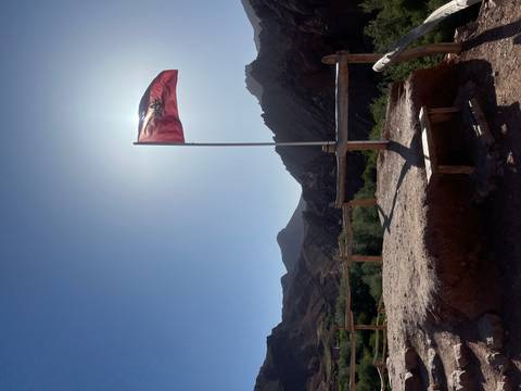 A Moroccan flag flutters on a tall pole against a bright sky with rugged mountains silhouetted behind.
