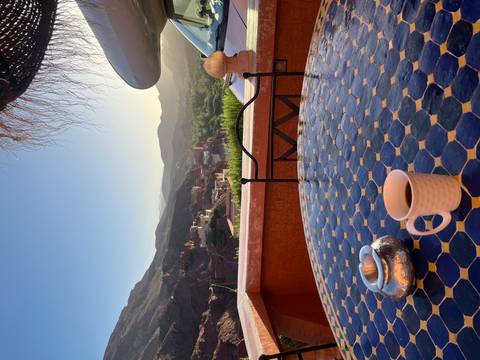 Morning view from a tiled terrace table with coffee overlooking a small village nestled in green mountains.