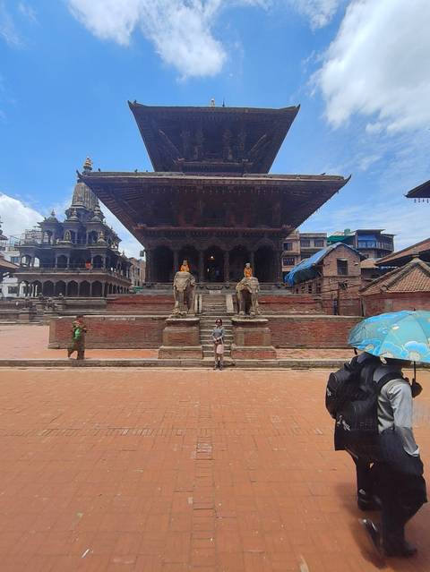 Stone temple with guardian elephant statues sits in an open square while a traveler poses in front.