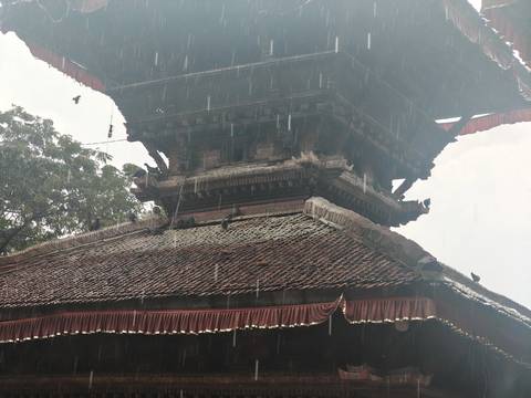 Close-up of a traditional Nepalese temple roof as rain falls heavily against the ornate woodwork.