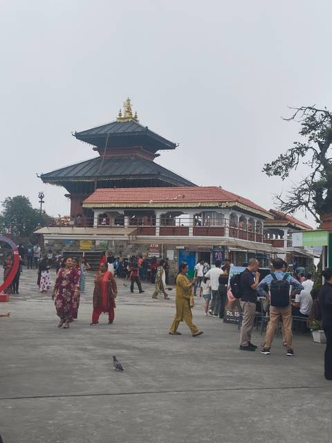 Busy hilltop temple complex with crowds of pilgrims and tourists milling around under cloudy skies.