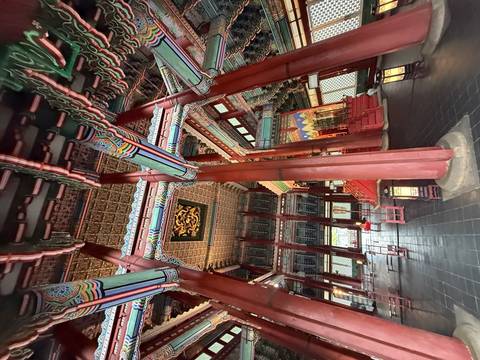 Ornate wooden columns and vibrant painted ceilings inside a grand Korean palace throne hall.