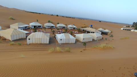 Aerial view of a desert luxury tent camp arranged in neat rows on golden dunes.