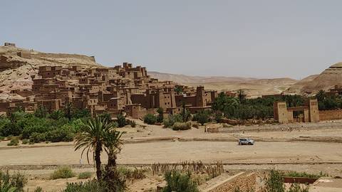Historic earthen ksar of Ait Benhaddou rises above a green oasis against a barren desert backdrop.
