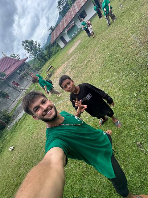 Smiling volunteer taking selfie with local child on grassy field in rural Laos.