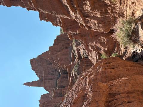 A jagged sandstone pinnacle dominates the arid canyon landscape under bright sunshine.