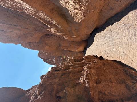 Sunlit sandy trail curves through high red canyon walls with clear blue sky above.