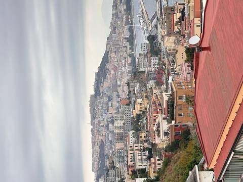 Colorful hillside buildings cascade toward the bay in Naples beneath a cloudy sky.