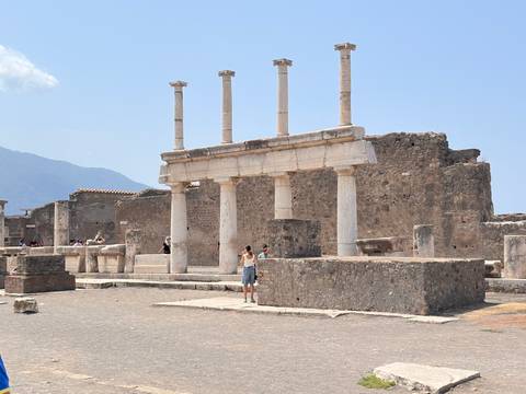 Ancient columns and stone walls in the forum of Pompeii with visitors exploring the ruins.